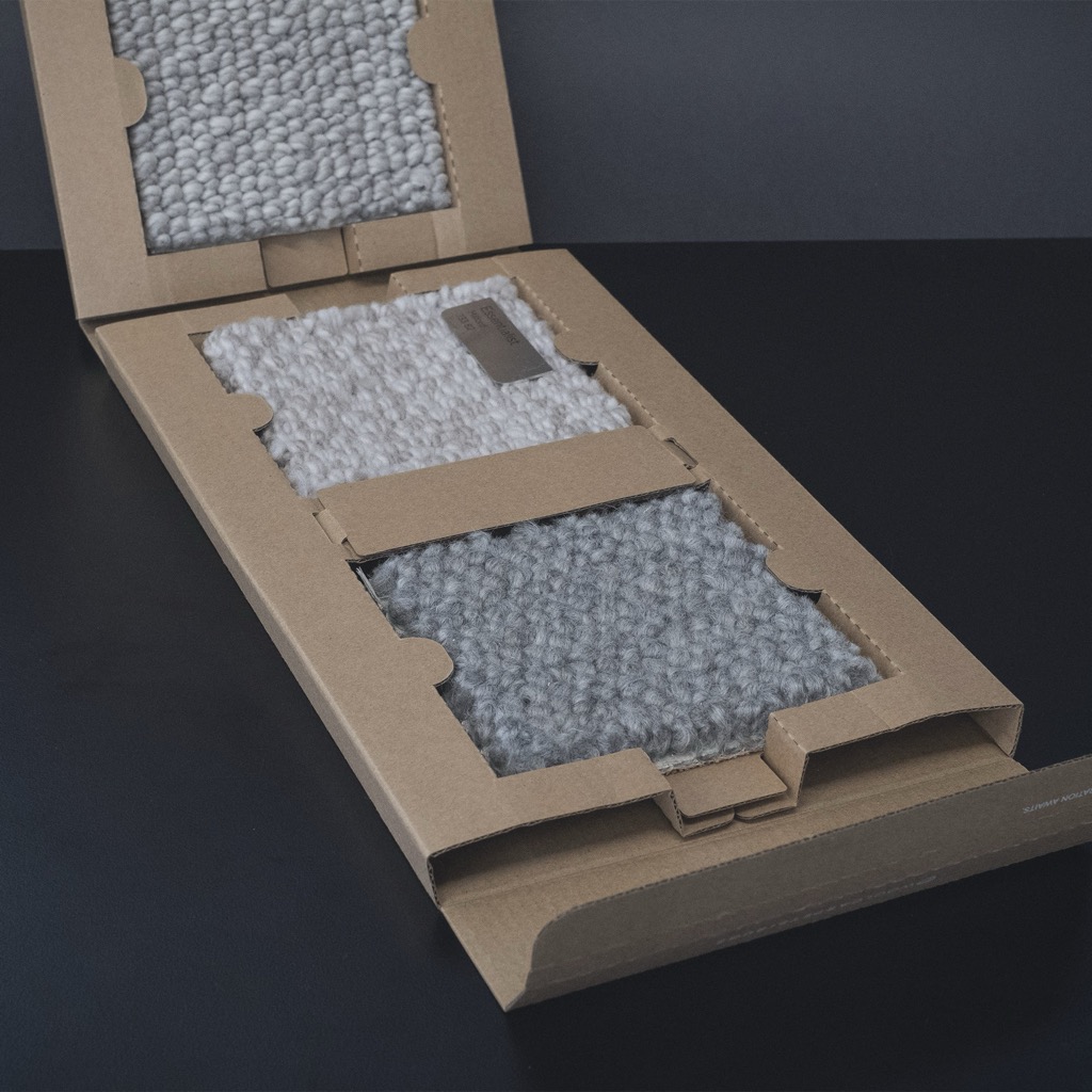 Kraft corrugate sample folder with die-cut retention windows holding wool carpet swatches.